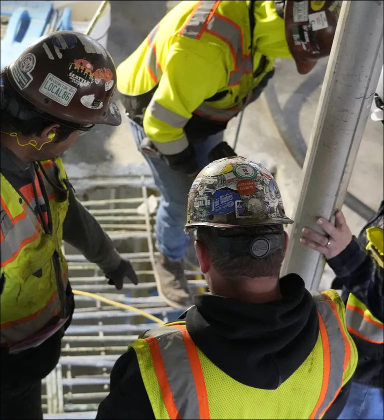 Close-up of construction workers in safety gear reviewing rebar placement and post-tensioning cables on a concrete slab.